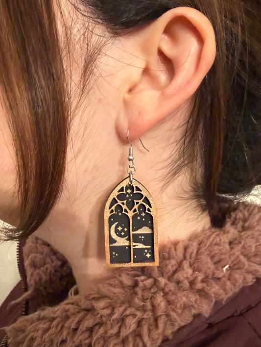 Close-up of an ear wearing a decorative earring with a gothic window night sky design.